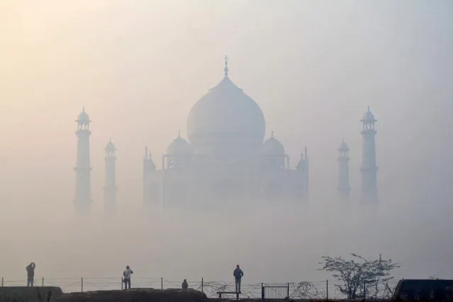 People exercise against the backdrop of Taj Mahal covered with fog on a cold winter morning in Agra on January 1, 2023. (Photo by Pawan Sharma/AFP Photo)