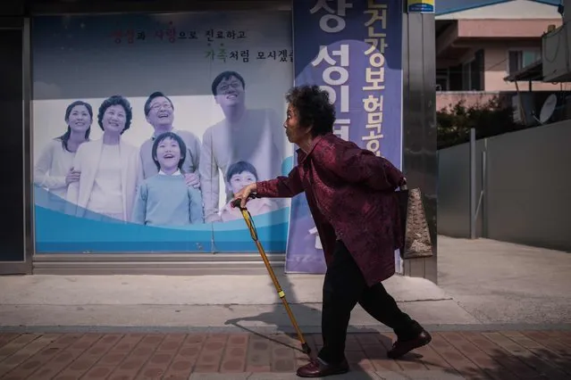 In a photo taken on May 27, 2016 an elderly woman walks past a poster at a health centre in Gunwi, some 200 kilometres south of Seoul. By 2030, a quarter of all South Koreans will be over 65 years old, and the overall population is expected to peak at around 52 million the same year before entering a period of steady decline. This so-called "silver tsunami" poses a major challenge for Asia's fourth-largest economy as the young, working-age population declines and the cost of caring for the elderly escalates. And in remote, rural communities like Gunwi, which lies some 200 kilometers southeast of Seoul, the trend is exacerbated by a youth exodus to the cities for work. (Photo by Ed Jones/AFP Photo)