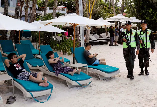 Policemen walk past tourists, one day before the temporary closure of the holiday island Boracay, in the Philippines April 25, 2018. (Photo by Erik De Castro/Reuters)
