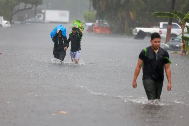 (L-R) Denis Mendez, Isain Lopez, and Santiago Rojas walk through a flooded street on April 13, 2023 in Fort Lauderdale, Florida. Nearly 26 inches of rain fell on Fort Lauderdale over a 24-hour period, with more expected throughout the day, according to the National Weather Service. Fort Lauderdale-Hollywood International Airport traffic is closed until 5 a.m. Friday. (Photo by Joe Raedle/Getty Images)