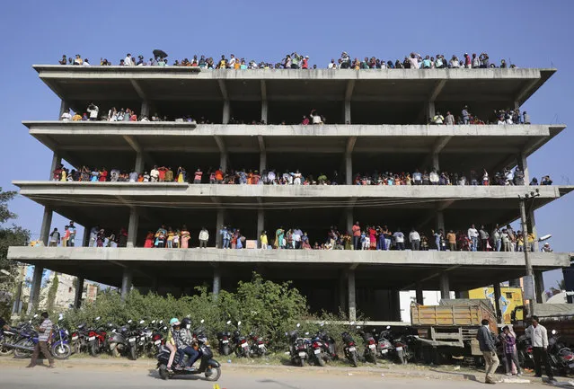 People stand on an under construction building outside Yelahanka air base and watch Indian Air Force Suryakiran aircrafts perform aerobatic maneuvers on the second day of Aero India 2021 in Bengaluru, India, Thursday, February 4, 2021. Aero India is a biennial event with flying demonstrations and commercial pavilions where aviation companies display their products and technology. (Photo by Aijaz Rahi/AP Photo)
