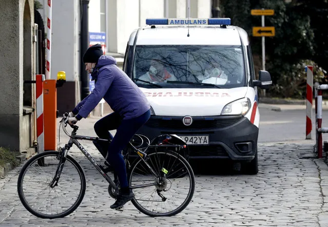 A cyclist passes in front of an ambulance by an infectious diseases hospital in Warsaw, Poland, on Thursday, March 25, 2021. Amid a sharp spike in new infections and hospitalizations that are bringing the health care to its limits, Poland has stepped up pandemic measures for two weeks starting Saturday, including fewer people to be allowed into churches at the holiday time. (Photo by Czarek Sokolowski/AP Photo)