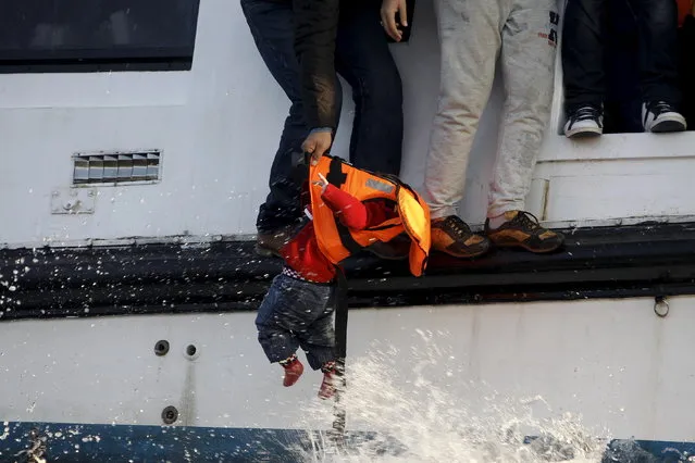 A refugee prepares to hand over a toddler to a volunteer lifeguard as a half-sunken catamaran carrying around 150 refugees, most of them Syrians, arrives after crossing part of the Aegean sea from Turkey on the Greek island of Lesbos, October 30, 2015. There were no casaulties amongst the refugees who were travelling on the catamaran, according to a Reuters witness. (Photo by Giorgos Moutafis/Reuters)