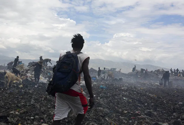 In this August 27, 2018 photo, Changlair Aristide walks across the Truitier landfill wearing his soccer uniform after a day of scavenging for useful items to use or sell, on his way to hang out with friends in the Cite Soleil slum of Port-au-Prince, Haiti. From his earnings at the dump site, Aristide bought two pigs and built a house made of corrugated steel just beyond the landfill's edge, where he lives with his wife and three of his kids. (Photo by Dieu Nalio Chery/AP Photo)