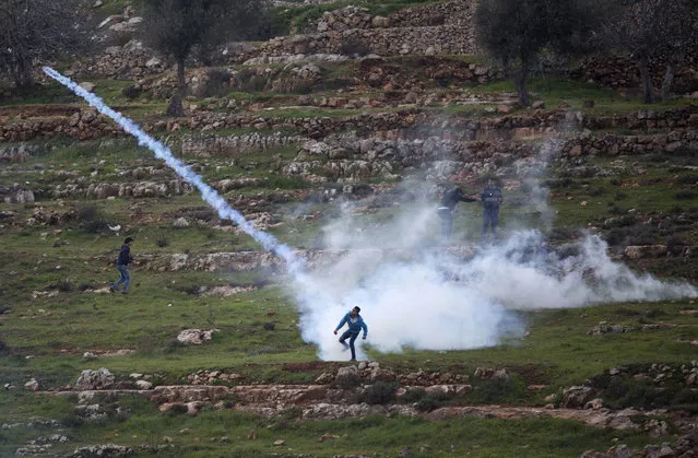 A Palestinian demonstrator throws back a tear gas canister that was fired by Israeli troops during  demonstration a calling for the release of Palestinian journalist Mohammed al-Qeq, outside Ofer military prison near the West Bank city of Ramallah, Thursday, February 11, 2016. Al-Qeq has refused food for over 70 days to protest his six-month imprisonment without trial or charges, an Israeli practice known as administrative detention. (Photo by Majdi Mohammed/AP Photo)