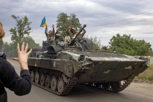 In this photograph taken on September 20, 2022 a local resident greets Ukrainian soldiers riding an armoured personnel carrier in Mala Komyshuvakha, near Izyum, Kharkiv region. (Photo by Yevhen Titov/AFP Photo)