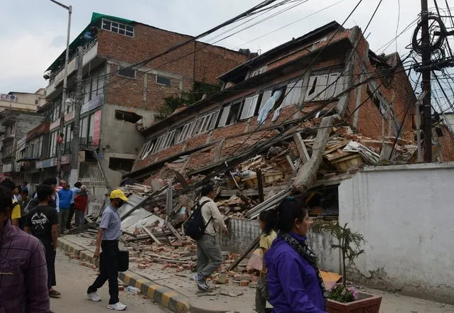 Nepalese people walk past a collapsed bullding in Kathmandu after an earthquake on April 25, 2015. (Photo by Prakash Mathema/AFP Photo)