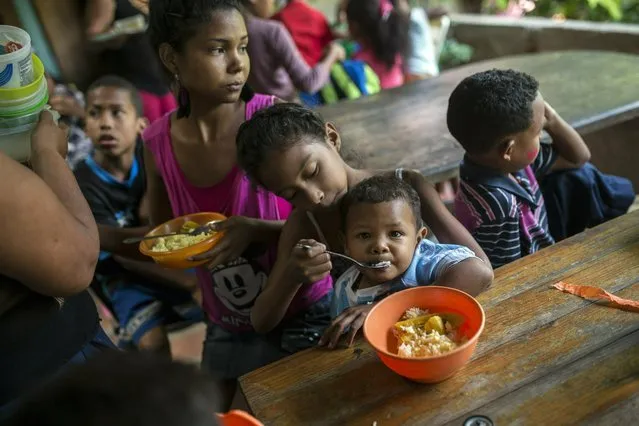 Eight-year-old Franyelis feeds her baby brother Joneiber as their mother Francibel Contreras holds a bowl of scrambled eggs and rice, at a soup kitchen in the Petare slum, Caracas, Venezuela. Contreras brings her three malnourished children to the soup kitchen in the dangerous hillside slum where they scoop in spoonfuls of food in what could be their only meal of the day. (Photo by Rodrigo Abd/AP Photo)