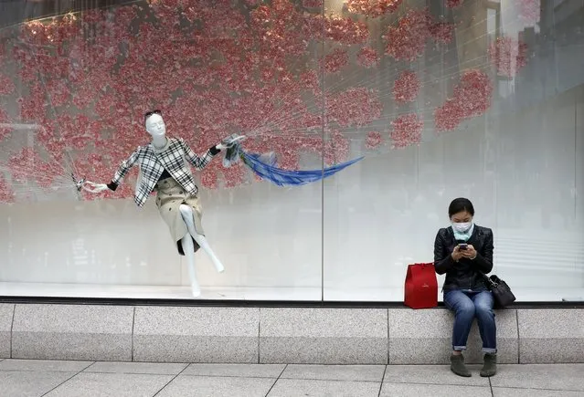 A woman uses her phone as she sits in front of a shop window in the Ginza shopping district in Tokyo, Japan, March 24, 2016. Japan's consumer inflation was flat in the year to February as low energy costs and weak consumption put a lid on price growth, keeping the central bank under pressure to top up stimulus even after easing policy less than two months ago. (Photo by Thomas Peter/Reuters)