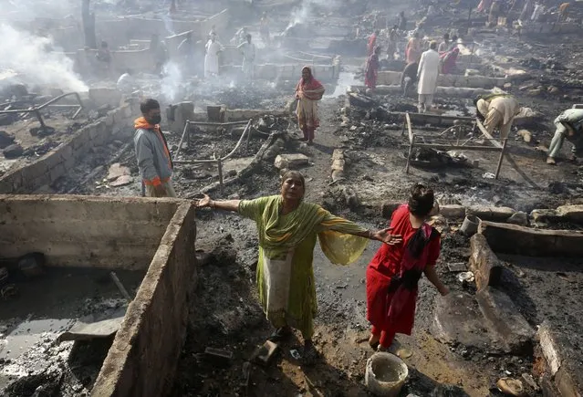 A woman griefs while she and others collect their belongings in Karachi, Pakistan, Saturday, November 20, 2021, following a fire that gutted hut homes. Scores of huts were burnt to ashes as the fire erupted making dozens of families homeless in a slum of Karachi, local media reported. (Photo by Fareed Khan/AP Photo)