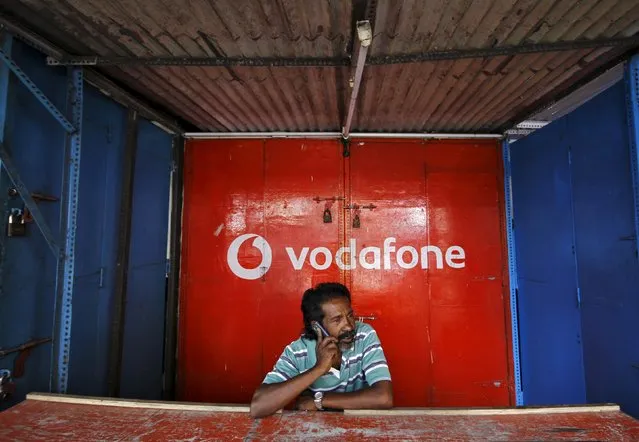 A retail shop owner speaks on his mobile phone outside his closed shop shutters painted with an advertisement for Vodafone at a market in the southern Indian city of Chennai December 30, 2013. (Photo by Reuters/Babu)