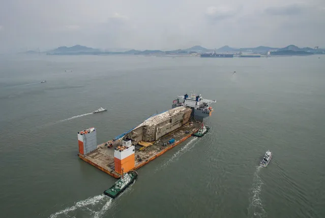 This aerial general view shows the wreck of the Sewol ferry mounted on a semi- submersible barge during its arrival at a port in Mokpo on March 31, 2017. The salvaged wreck of South Korea' s Sewol ferry finally reached port on March 31, nearly three years after setting out on a doomed voyage that killed more than 300 people. (Photo by Ed Jones/AFP Photo)