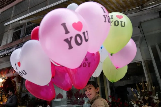 An Afghan boy gestures as he sells Valentine's Day balloons on a street in Kabul, Afghanistan, Sunday, February 13, 2022. (Photo by Hussein Malla/AP Photo)