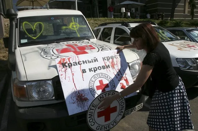 A demonstrator adjusts a placard reading “Red Cross is in blood” on a vehicle of the Red Cross during a protest to demand what protesters say is true information from the Organisation for Security and Co-operation in Europe (OSCE) about the shelling in Donetsk, Ukraine, July 23, 2015. (Photo by Igor Tkachenko/Reuters)