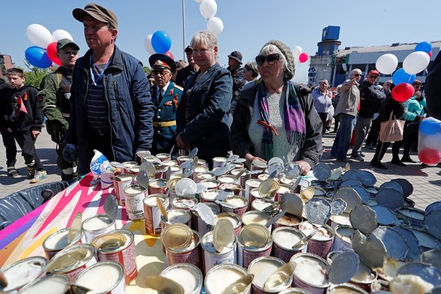 People stand next to a table with tins of canned stewed meat during a ceremony, marking the 77th anniversary of the victory over Nazi Germany in World War Two, during Ukraine-Russia conflict in the southern port city of Mariupol, Ukraine May 9, 2022. (Photo by Alexander Ermochenko/Reuters)
