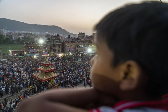 A Nepalese boy watches devotees pull down the “lingo” a long wooden pole symbolising a phallus during Biska Jatra festival in Bhaktapur, Nepal, Thursday, April 14, 2022. During this festival, also regarded as Nepalese New Year, images of Hindu god Bhairava and his female counterpart Bhadrakali are enshrined in two large chariots and pulled to an open square after which rituals and festivities are performed. (Photo by Niranjan Shrestha/AP Photo)