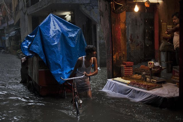 An Indian sweets vendor, right, shouts at a laborer who is pulling a cart through a street flooded due to monsoon rains in New Delhi, India, Sunday, August 10, 2014. The vendor was reacting angrily since the ripples created by the cart's movement was causing the floodwater to enter his shop. (Photo by Tsering Topgyal/AP Photo)