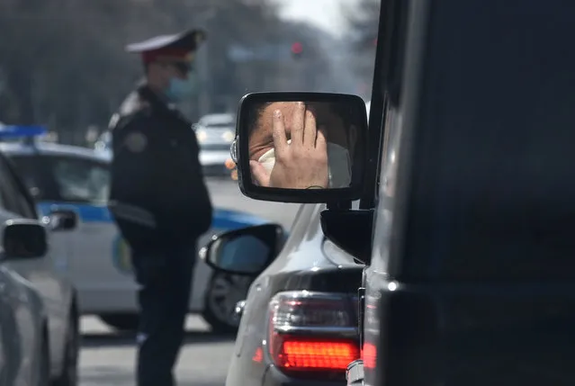 A person wearing a protective mask, used as a preventive measure against coronavirus disease (COVID-19), is reflected in the side mirror of a car near a Kazakh law enforcement officer in Almaty, Kazakhstan on March 30, 2020. (Photo by Mariya Gordeyeva/Reuters)