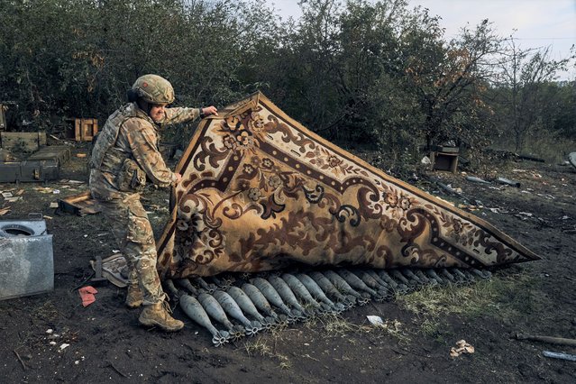 A Ukrainian soldier lifts a carpet that covered the Russian ammunition in Izium, Kharkiv region, Ukraine, Tuesday, September 13, 2022. (Photo by Kostiantyn Liberov/AP Photo)