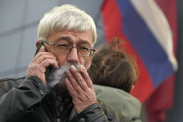 Oleg Orlov, a member of the Board of the International Historical Educational Charitable and Human Rights Society “Memorial” (International Memorial) speaks by phone and smokes after a court hearing, with the Russian flag in the background, in Moscow, Russia, Friday, October 7, 2022. On Friday, Oct. 7, 2022 the Nobel Peace Prize was awarded to jailed Belarus rights activist Ales Bialiatski, the Russian group Memorial and the Ukrainian organization Center for Civil Liberties. (Photo by Alexander Zemlianichenko/AP Photo)