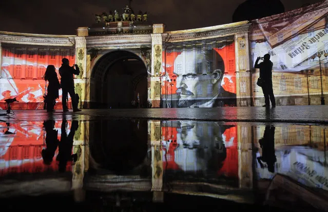 People look at a portrait of Soviet Union founder Vladimir Lenin drawn in light at Dvortsovaya (Palace) Square during a light show marking the centenary of the Bolshevik Revolution in St.Petersburg, Russia, Saturday, November 4, 2017. (Photo by Dmitri Lovetsky/AP Photo)