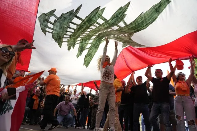 Supporters of Lebanese President Michel Aoun hold up a giant Lebanese flag as he delivers a speech outside the presidential palace in Baabda, east of Beirut, Lebanon, Sunday, October 30, 2022. Aoun left Lebanon's presidential palace Sunday marking the end of his six-year term without a replacement, leaving the small nation in a political vacuum that is likely to worsen its historic economic meltdown. (Photo by Bilal Hussein/AP Photo)