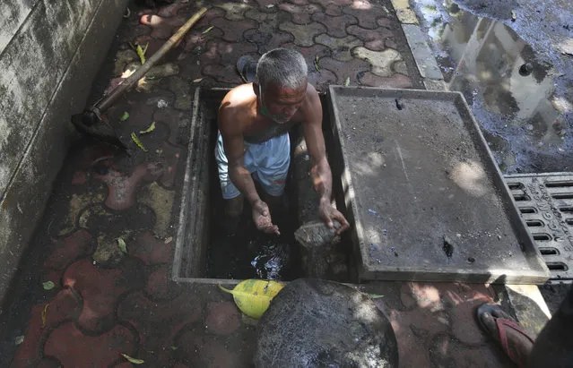 A laborer cleans a manhole on a sidewalk in Mumbai, India, Wednesday, June 10, 2020. While 2019 was the worst year on record for global dengue cases, experts fear an even bigger surge is possible because their efforts to combat it were hampered by restrictions imposed during the coronavirus pandemic. (Photo by Rafiq Maqbool/AP Photo)