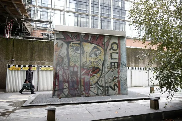A man walks near a piece of the Berlin Wall in La Defense business district in Courbevoie October 16, 2014. The municipality of Courbevoie bought the piece of wall for 300.000 Deutsche Marks in 1990. The segment shows a painting of Kiddy Citny. (Photo by Charles Platiau/Reuters)