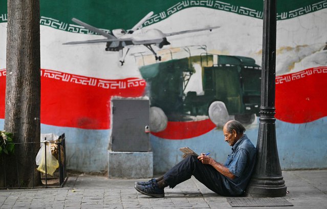 A man writes on a piece of cardboard while sitting on the ground in a Caracas square on January 20, 2025. (Photo by Juan Barreto/AFP Photo)