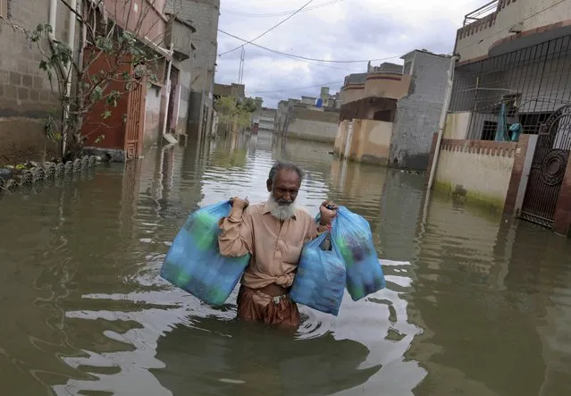 A man carries goods as he wades through flooded street after heavy monsoon rains, in Karachi, Pakistan, Wednesday, August 26, 2020. Pakistan's military said it will deploy rescue helicopters to Karachi to transport some 200 families to safety after canal waters flooded the city amid monsoon rains. (Photo by Fareed Khan/AP Photo)