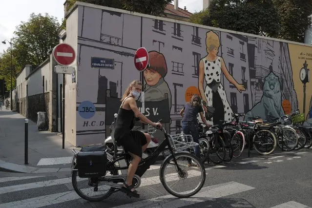 A woman, wearing a protective face mask as a precaution against the coronavirus, rides her bicycle front of a mural representing late film director Agnes Varda, in Paris, Friday, September 11, 2020. (Photo by Francois Mori/AP Photo)