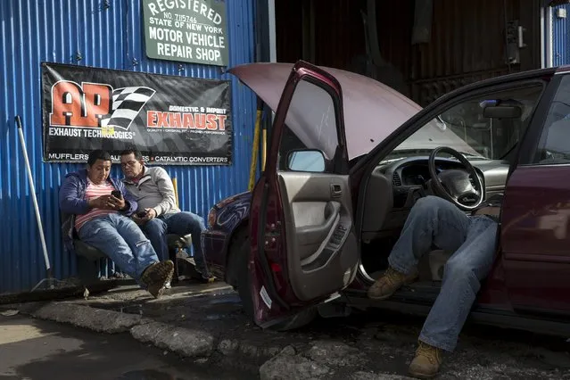 Men look at a cellular device as a worker tends to an automobile in the Willets Point area of Queens in New York October 29, 2015. (Photo by Andrew Kelly/Reuters)