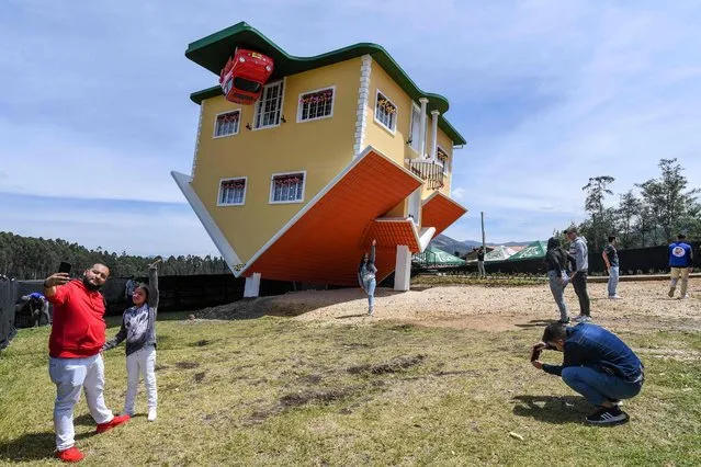 People pose for photos outside the upside-down house, in Guatavita, near Bogota, on January 29, 2022. The house was designed by its Austrian owner Fritz Schall. (Photo by Juan Barreto/AFP Photo)