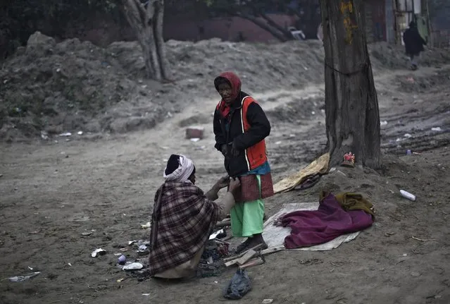A man helps a woman to wear a donated jacket on a cold winter morning on the banks of the river Yamuna in New Delhi December 23, 2014. (Photo by Adnan Abidi/Reuters)