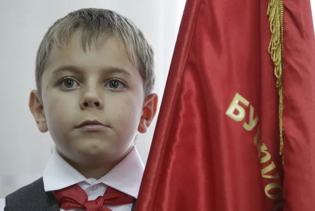A boy, holding a flag and wearing red neckerchief, a symbol of the Pioneer Organization, attends a ceremony for the inauguration of 18 new members at a local school in the southern settlement of Kazminskoye in Stavropol region, Russia, November 19, 2015. (Photo by Eduard Korniyenko/Reuters)