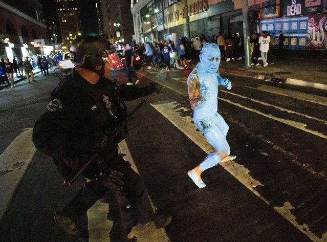 A person covered in blue paint runs from a police officer as fans celebrate on streets after the Los Angeles Dodgers won against the New York Yankees in the baseball World Series Wednesday, October 30, 2024, in Los Angeles. (Photo by Ethan Swope/AP Photo)