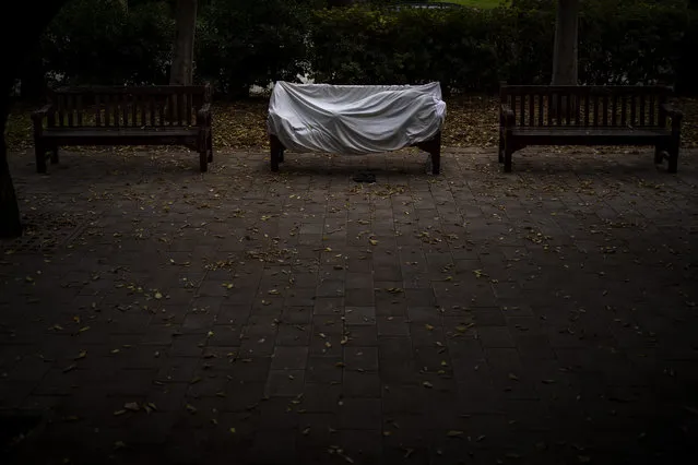 A homeless man covered by a sheet sleeps on a bench at a public park in Barcelona, Spain, Sunday, December 20, 2020. (Photo by Emilio Morenatti/AP Photo)