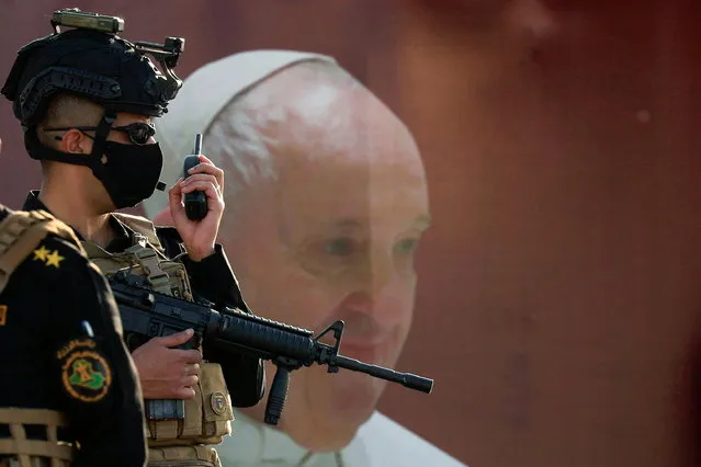 A member of Iraqi security forces stands guard near a poster of Pope Francis ahead of his arrival to the Syro-Catholic Cathedral of “Our Lady of Salvation” in Baghdad, Iraq on March 5, 2021. (Photo by Thaier Al-Sudani/Reuters)