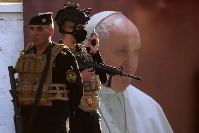 Members of Iraqi security forces stand guard near a poster of Pope Francis ahead of his arrival to the Syro-Catholic Cathedral of “Our Lady of Salvation” in Baghdad, Iraq on March 5, 2021. (Photo by Thaier Al-Sudani/Reuters)