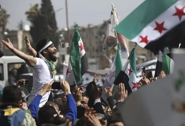 An anti-Syrian government protester shouts slogans as others wave revolutionary flags, to mark 10 years since the start of a popular uprising against President Bashar Assad's rule, that later turned into an insurgency and civil war, In Idlib, the last major opposition-held area of the country, in northwest Syria, Monday, March 15, 2021. (Photo by Ghaith Alsayed/AP Photo)