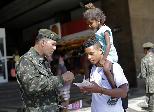 An army soldier explain how to combat the Aedes aegypti mosquito that spreads the Zika virus, at the Central station, in Rio de Janeiro, Brazil, Saturday, February 13, 2016. More than 200,000 army, navy and air force troops are fanning out across Brazil to show people how to eliminate the Aedes aegypti mosquito that spreads the Zika virus, which many health officials believe is linked to severe birth defects. The nationwide offensive is part of President Dilma Rousseff's declared war on the virus that has quickly spread across the Americas. (Photo by Silvia Izquierdo/AP Photo)
