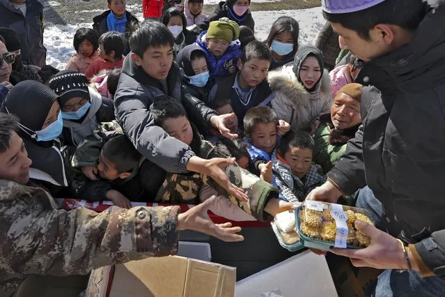 Quake victims scramble to get snack foods from a volunteer at a temporary settlement in Chenjiacun village in Jishishan county in northwest China's Gansu province on Wednesday, December 20, 2023. Hundreds of temporary housing units were being set up in northwest China on Thursday for survivors of an earthquake, according to state media reports. (Photo by Chinatopix via AP Photo)