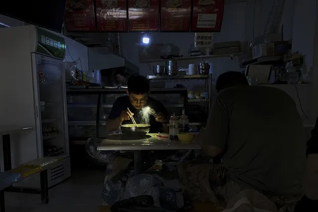 A man uses his smartphone flashlight to light up his bowl of noodles as he eats his breakfast at a restaurant during a blackout in Shenyang in northeastern China's Liaoning Province, Wednesday, September 29, 2021. People ate breakfast by flashlight and shopkeepers used portable generators Wednesday as power cuts imposed to meet official conservation goals disrupted manufacturing and daily life. (Photo by Olivia Zhang/AP Photo)