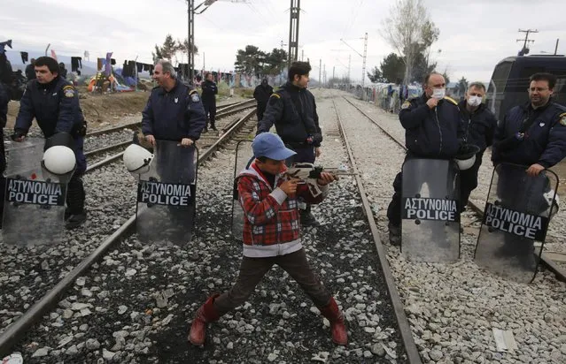 A boy plays with a toy gun in front of the policemen as other migrants block the railway track at the Greek-Macedonian border, near the village of Idomeni, Greece March 12, 2016. (Photo by Stoyan Nenov/Reuters)