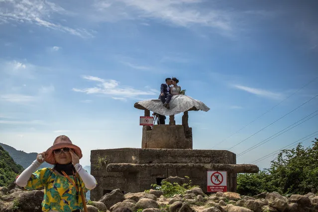 A tourist walks past a Vietnamese couple on an old bunker posing for their wedding photos, at the highest point of Hai Van Pass, Vietnam, 05 June 2019. Hai Van Pass is around 21 km long mountain pass at an elevation of 496m above the sea level, located in Central Vietnam, between the popular tourist spots of Hoi An and Danang to the south and Hue to the north. The pass is considered as one of the most scenic hillside roads in Vietnam. (Photo by Roman Pilipey/EPA/EFE)