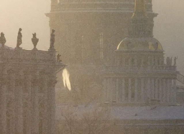 A worker throws snow from the roof of the Winter Palace during snowfall in St. Petersburg, Russia, Tuesday, January 11, 2022, with the Admiralty building and the St. Isaac's Cathedral in the background. (Photo by Dmitri Lovetsky/AP Photo)