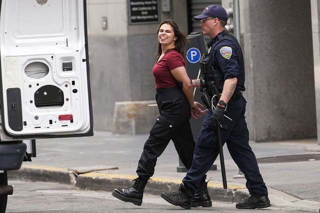 A pro-Palestinian demonstrator sticks her tongue out as she is escorted to a police vehicle outside a building housing the Israeli Consulate in San Francisco, Monday, June 3, 2024. Police arrested Palestinian supporters Monday who occupied the lobby of the building. (Photo by Jeff Chiu/AP Photo)