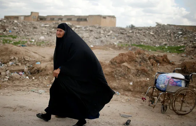 A displaced Iraqi woman who had fled her home walks past destroyed buildings at Hammam al-Alil south of Mosul, Iraq April 3, 2017. (Photo by Suhaib Salem/Reuters)