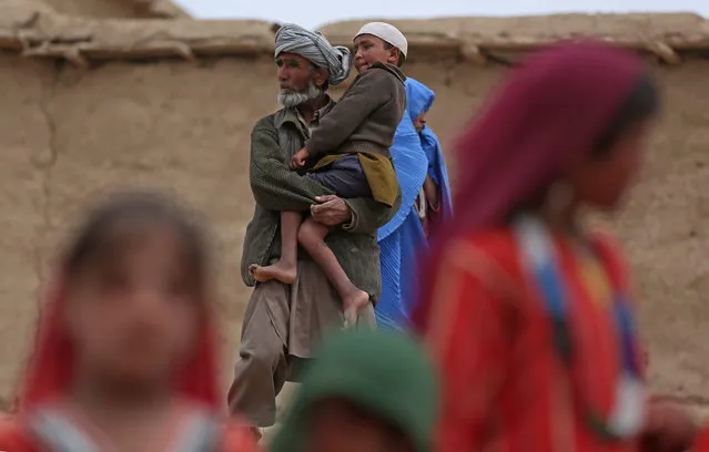 In this Sunday, May 4, 2014 photo, Afghan man, center, holds his son as he walks, near the site of Friday's landslide that buried Abi-Barik village in Badakhshan province, northeastern Afghanistan. Three days after the earth swept through his village, burying entire houses and hundreds of people, villagers are still digging in search for their loved ones. (Photo by Massoud Hossaini/AP Photo)