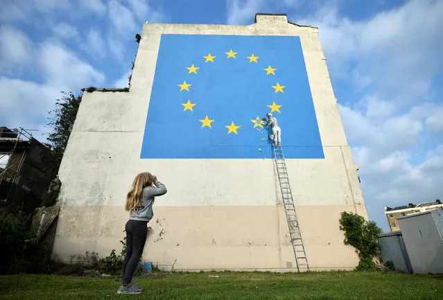A young girl looks at artwork attributed to street artist Banksy, depicting a workman chipping away at one of the 12 stars on the European Union, seen on a wall in the ferry port of Dover, Britain, May 7, 2017. (Photo by Hannah McKay/Reuters)